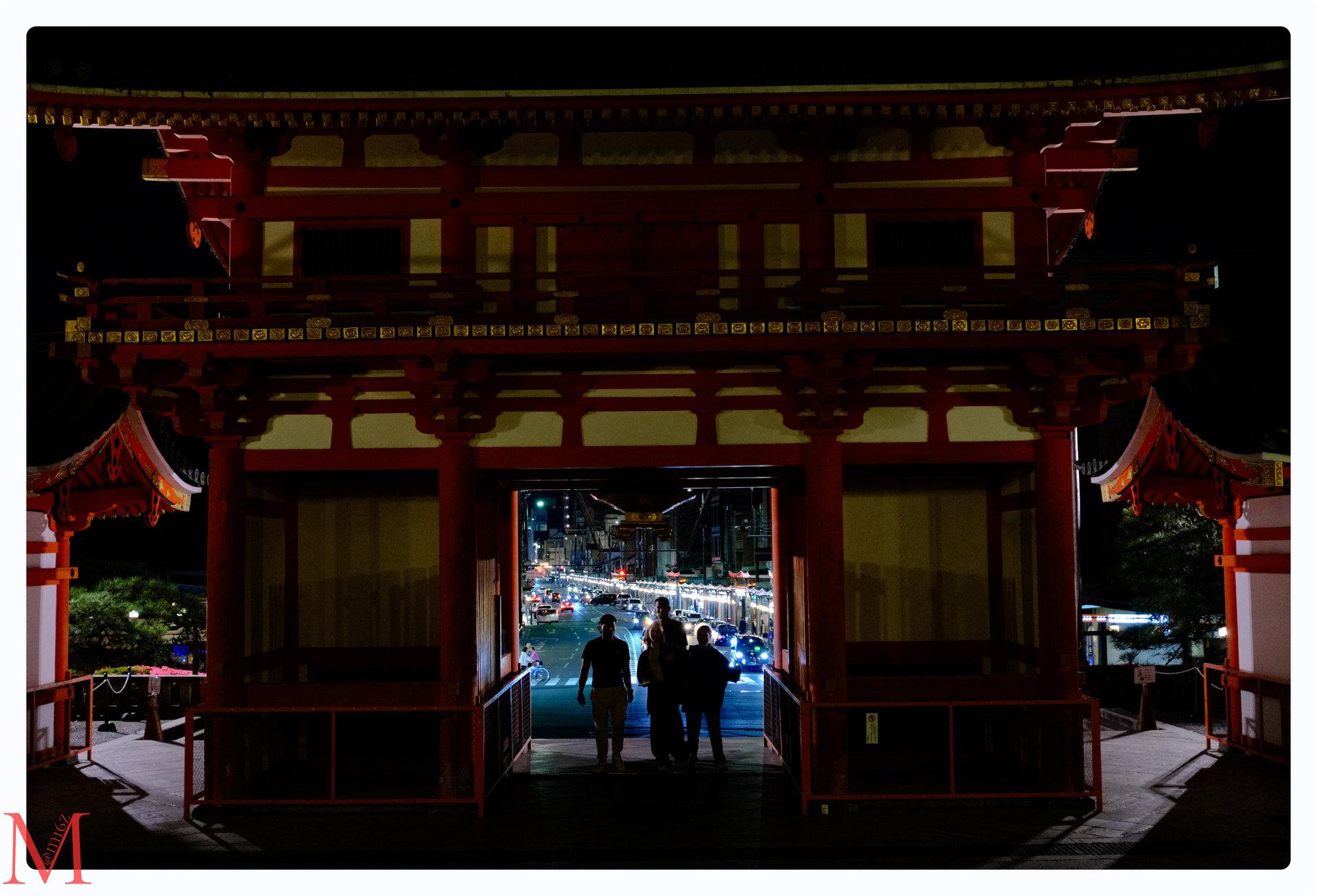 Yasaka-Schrein mit durchgehenden Menschen und einer belebten, beleuchteten Straße im Hintergrund.