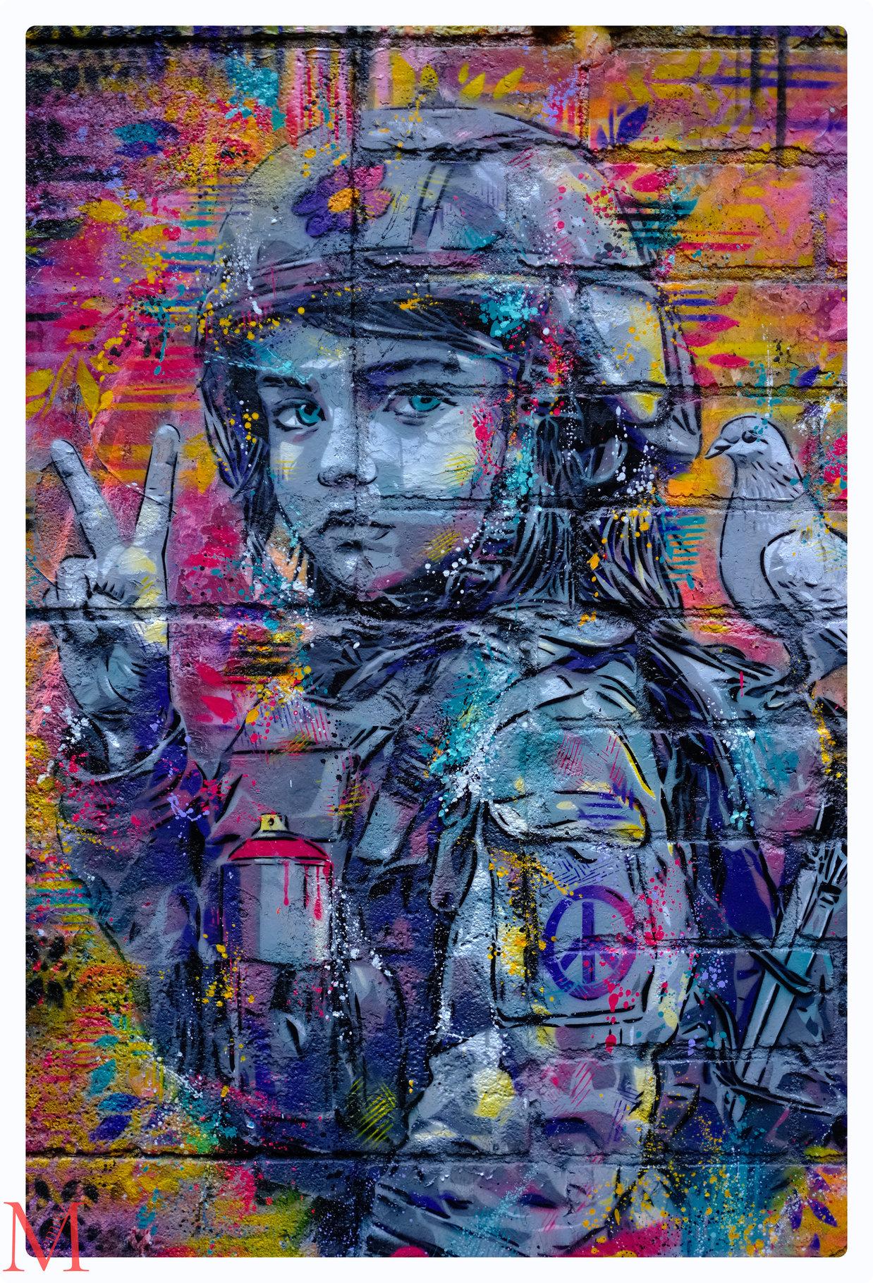 Kind in bunter Soldatenuniform mit Friedenssymbol-Aufnäher und weißer Taube macht das Victory-Zeichen.