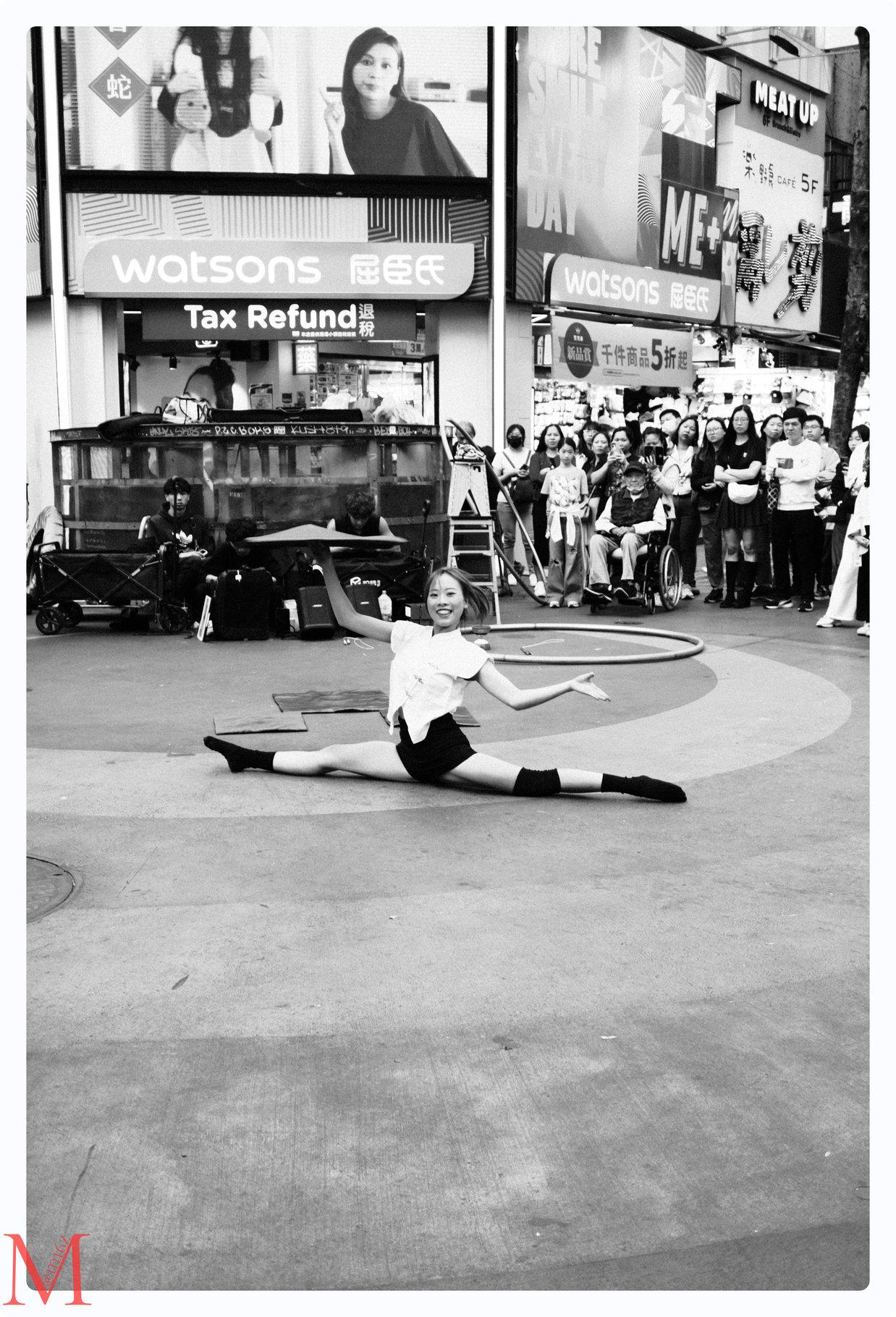 Straßenkünstlerin in Ximending macht einen Spagat, umgeben von jubelnden Zuschauern.