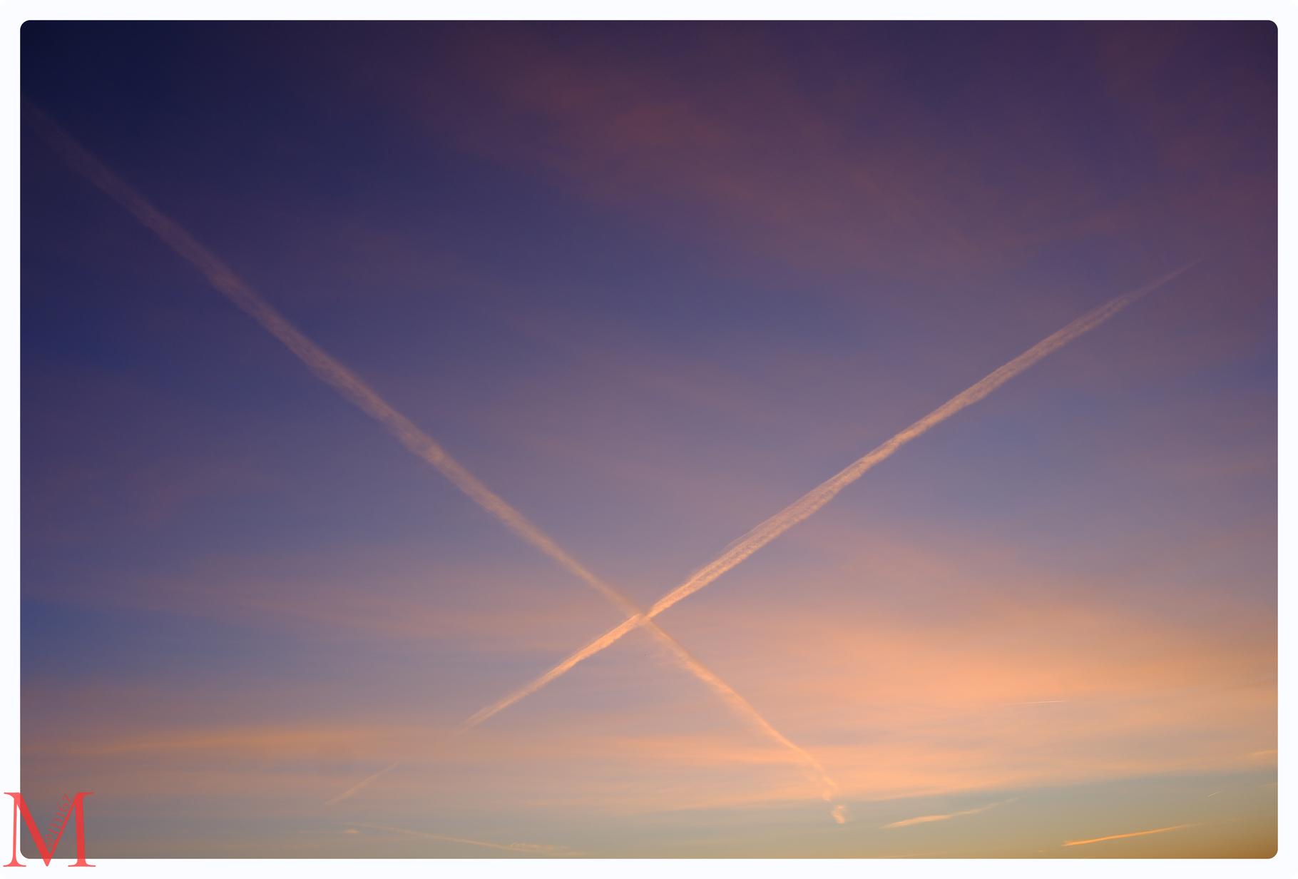 Sich kreuzende Kondensstreifen zweier Flugzeuge am roten Morgenhimmel.